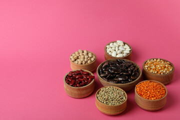 Bowls with different types of beans on pink background