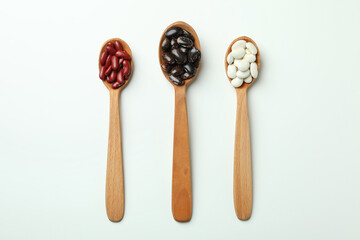 Spoons with different types of beans on white background