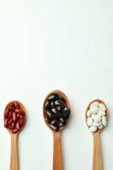 Spoons with different types of beans on white background