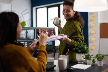 Creators drinking coffee and talking during office break sitting at desk in digital agency studio....