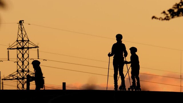 Young people on inline skates and skiing sticks at top of hill, girl run down then boy. Small athletes wear protections for ankles, knees and helmet for head