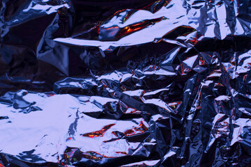 Abstract dark blue aluminum wrinkled foil background texture reflecting red and orange light.