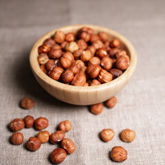 Wooden bowl with heap of tasty hazelnuts on table with gray linen tablecloth 