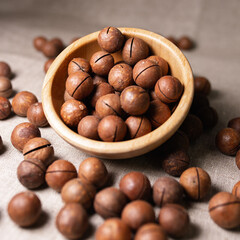 From above of brown macadamia nuts in shell in wooden bowl placed on table with linen tablecloth 
