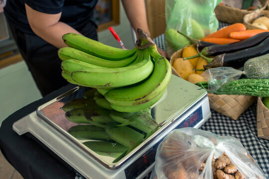 A vendor writes down the computed price of a raw lacatan banana on a digital weighing scale.