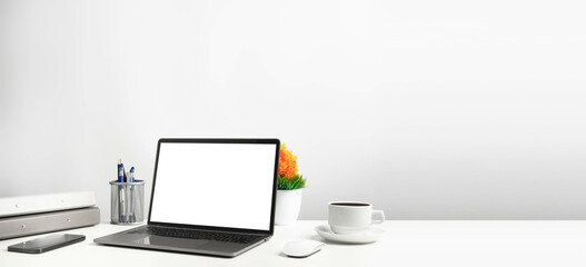 Blank white screen laptop on a white table in the office. Working concept using technology smartphones, notebook, coffee cup. Copy space on right for design or text, Closeup, Gray, and blur background