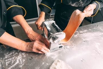 Two handy cooks are making pasta while using a special machine.