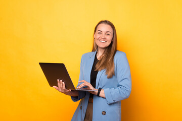 Cheerful business lady is holding and using laptop while smiling at the camera.