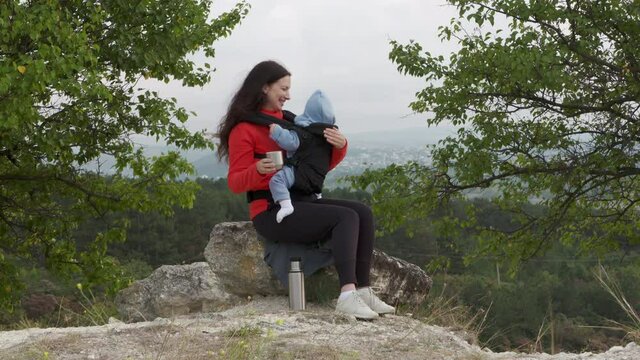 Woman with a baby in a sling ergo backpack traveling outdoor, family vacations adventure, mom with baby boy in infant kid carrier hiking. High quality 4k footage