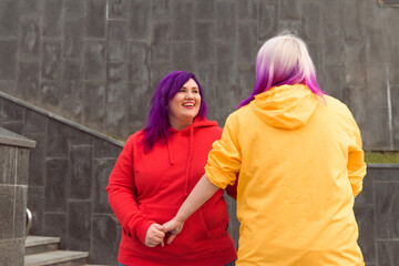 Obraz na płótnie Canvas happy young lesbians red and yellow color clothes embracing holding hands outdoors