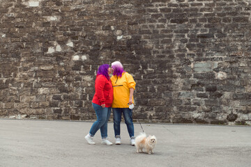 two color hair lesbian with small dog kissing at stone wall background city street