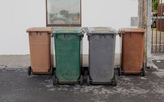 Four wheelie bins of different color and waste left in a street for collection. Waste and recycle management industry
