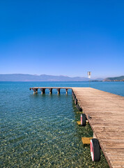 Empty wooden pier on the lake, blue sky, mountains background