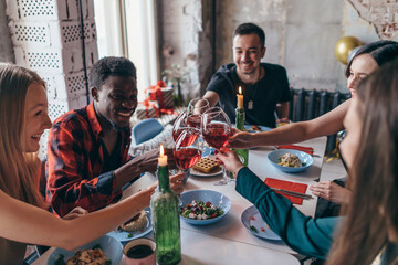Friends making toast clinking glasses above dinner table.