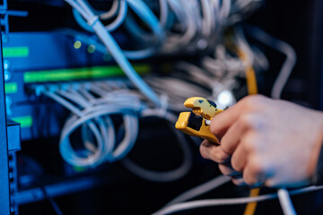 Hands of a technician using cable stripper on ethernet cable at data center, close-up. - obrazy, fototapety, plakaty