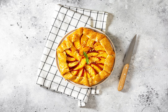 French galette or pie with peaches and in a white plate on a light gray culinary background top view. Summer homemade sweet pastries