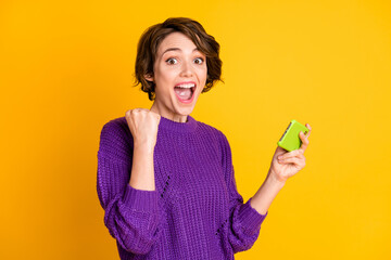 Photo portrait of cheerful screaming girl gamer holding phone vertically isolated on vivid yellow colored background