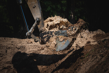 Fototapeta na wymiar Closeup of a backhoe loader equipment picking scraps and soil from underground by digging ground for construction during a bright and sunny day with water splashing out