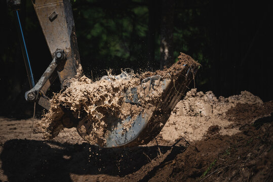 Closeup of a backhoe loader equipment picking scraps and soil from underground by digging ground for construction during a bright and sunny day with water splashing out