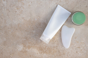 Beauty set. White gua sha scraper massager, foaming gel, cream on light textured surface. Copy space, flat lay. Concept beauty, self-care, face body care, home spa, well-being, preservation of youth