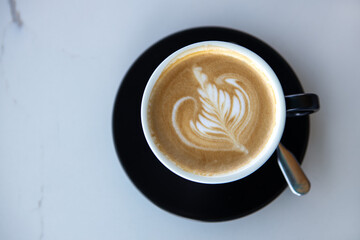 Cappuccino cup on black saucer on white marble table background. Latte design. Copy space. Top view, flat lay. Horizontal. For social media, food blog. Concept lactose free beverages, decaf coffee