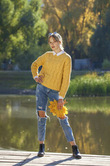 Young girl in a woolen sweater and torn jeans posing in an autumn park