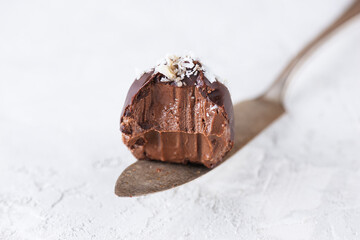 A piece of chocolate truffle with coconut flakes on a light background. Sugar, gluten and lactose free, healthy diet, vegan.