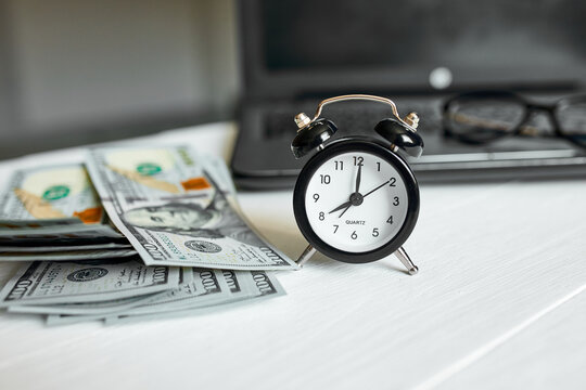 Modern workplace of laptop, clock, money, dollars banknote with copy space on white wooden background. Time for money.
