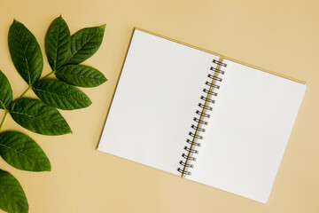 A blank notebook with leaves over the brown table. 