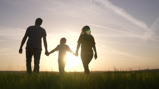 happy family. people in the park silhouette fun walk at sunset. mom dad and son walk holding hands in the park. happy kid family dream concept. parents and boy walking back silhouette