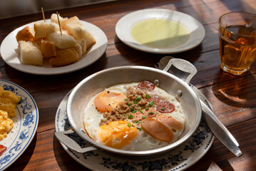 Fried egg with topping (sausage and ham) on pan, traditional breakfast on wooden table