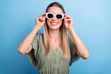 Photo of shiny charming young woman dressed green clothes arms dark eyewear smiling isolated blue color background