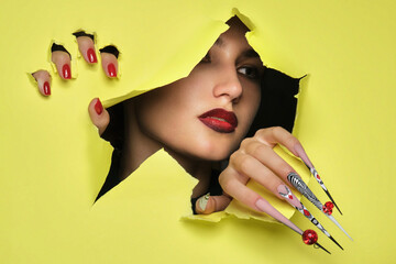 Portrait of a beautiful woman with art make up in glamorous style, creative long nails on a yellow...