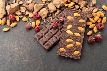 Cooking chocolate bars with almonds, raspberries, handmade sweets. Composition of bars and pieces of dark almond chocolate, raspberries on a black background, top view. Pastry craft on the table