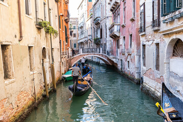 Fototapeta na wymiar Traditional gondolas on the narrow canal in Venice, Italy. Exploring beautiful Venice on water on a sunny day.
