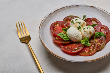 Caprese salad with red tomatoes, basil and mozzarella cheese in white plate and golden fork