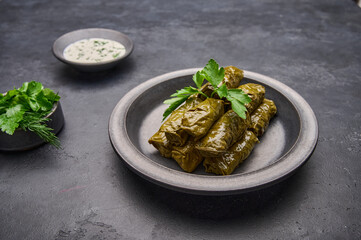 Dolma, parsley, saucepan with sour cream on ceramic color graphite plate on dark table, close up