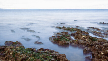 Fototapeta na wymiar Long exposure of waves coming in amongst rocks on a beach