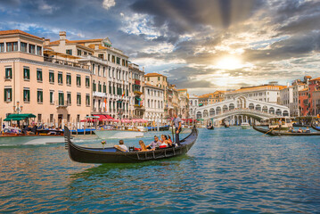 Venetian gondolier punting gondola through Grand canal waters of Venice Italy near Rialto bridge.