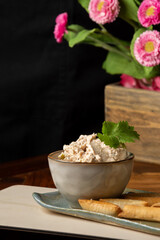 Close-up of bowl with turkey breast pate with cheese, mango, olives and muffins, on wooden table, dark background with flowers, vertical