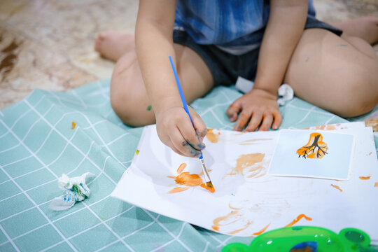 Focus on hands on paper. Children use paintbrushes to paint watercolors on paper to create their imagination and enhance their learning skills.