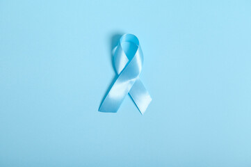 Flat lay of a blue satin ribbon, symbolic bow color raising awareness in diabetes day on blue colored background with copy space for ad, 14 November. World diabetes day awareness concept.