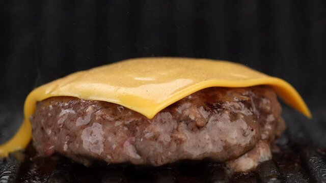 Cooking beef patty for burger with cheddar cheese on grill. Making Tasty Hamburger. 4K UHD video