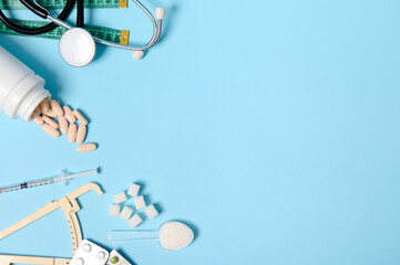 Scattered pharmaceutical pills, blisters of tablets, insulin syringe, stethoscope, caliper, measuring tape and refined sugar on blue background, copy space for Diabetes Awareness Day, 14 November