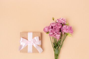 Gift box with tied bow and bouquet of eustoma flowers on a beige background. Minimal festive compisition with copyspace.