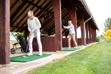 Senior people enjoying their retirement and practicing long shots on golf course.