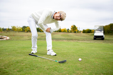Female senior golfer having health problems and knee pain on golf training.