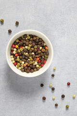Assorted multicolored colorful papper corn spice in white bowl on grey background vertical layout.