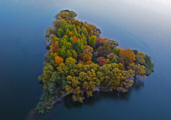 Beautiful colorful autumn island in the shape of a triangle. Forest trees on the lake