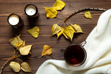 Tea plaid yellow branch leaves and candles over brown wooden background. Autumn cozy mood.